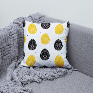 Poduszka ustawiona na kanapie obok szarego pleda jako wielkanocna dekoracja