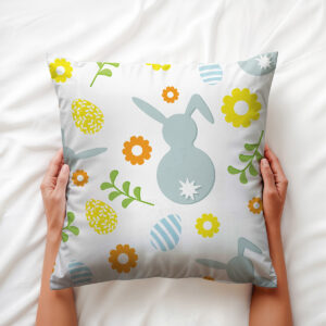 Zbliżenie na poduszkę trzymaną dłońmi, widoczny motyw zajączka i pisanek