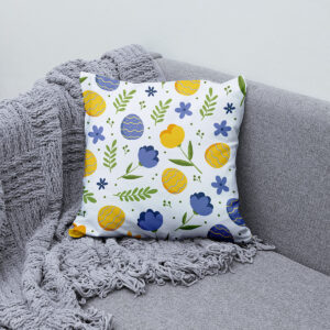 poduszka z pisankami i kwiatami ułożona na szarej kanapie obok pleda