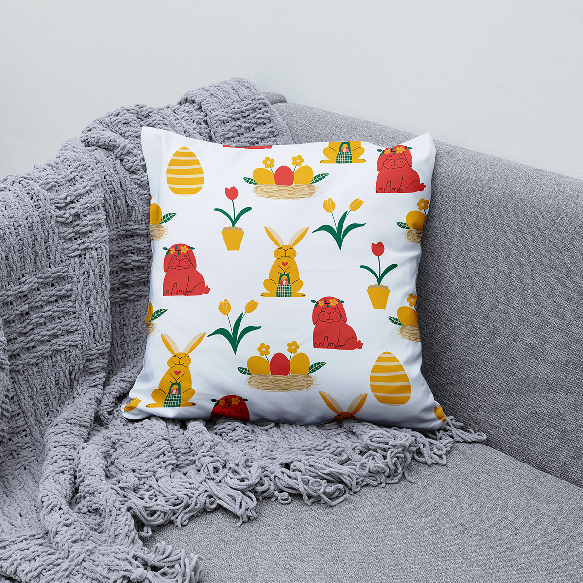 Poduszka ułożona na kanapie obok szarego koca, prezentująca dekoracyjny motyw