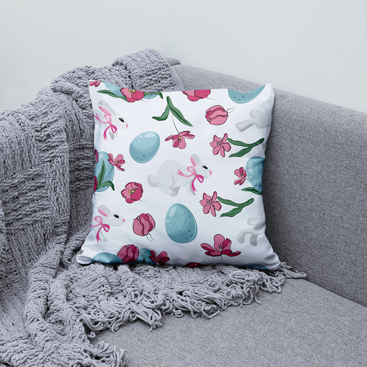 Poduszka ułożona na kanapie jako dekoracja, widoczne tulipany i zielone listki