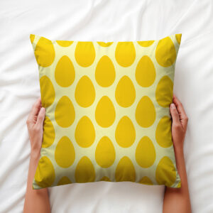 Poduszka trzymana obiema rękami na białej pościeli, widok z góry pokazujący powtarzalny motyw jajek