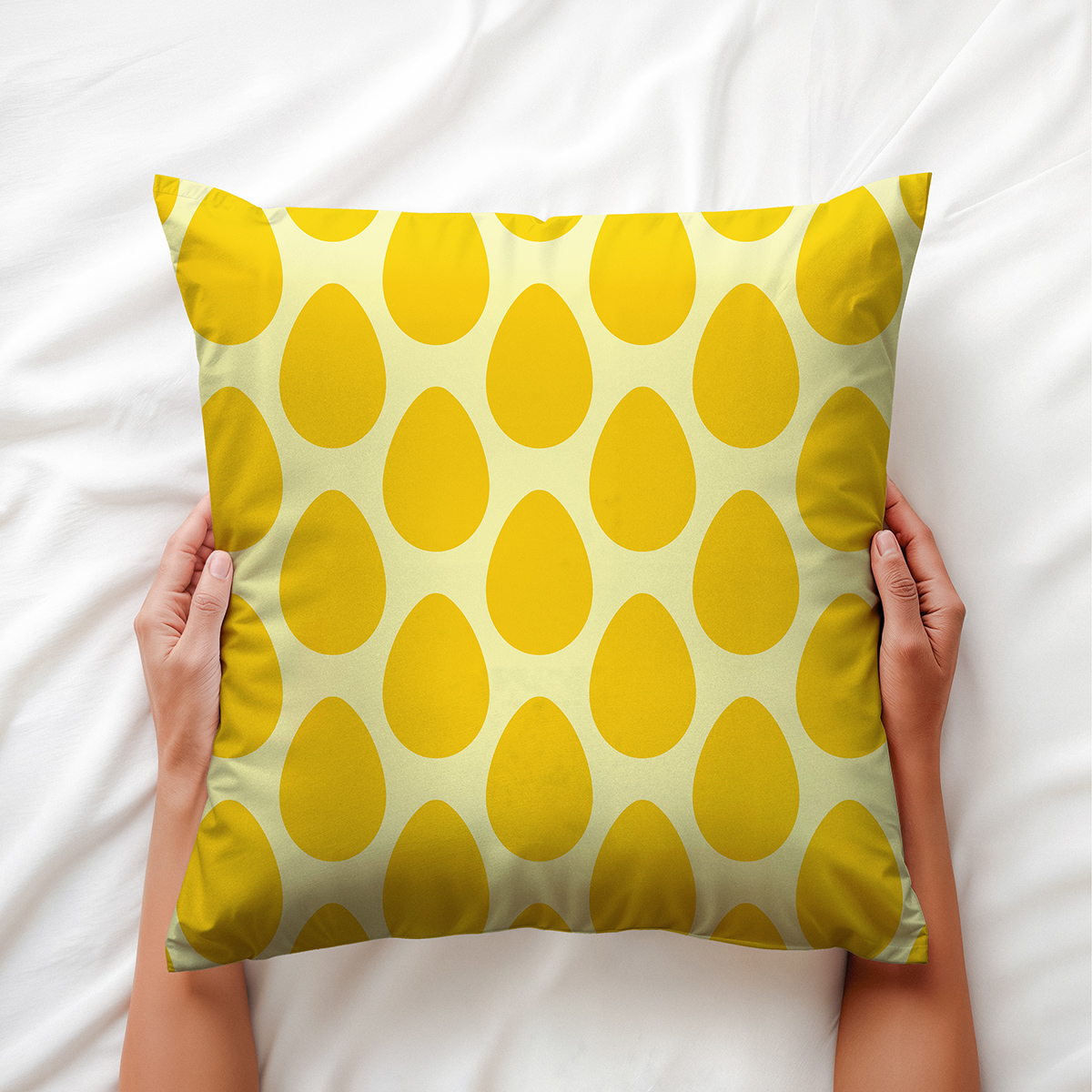 Poduszka trzymana obiema rękami na białej pościeli, widok z góry pokazujący powtarzalny motyw jajek