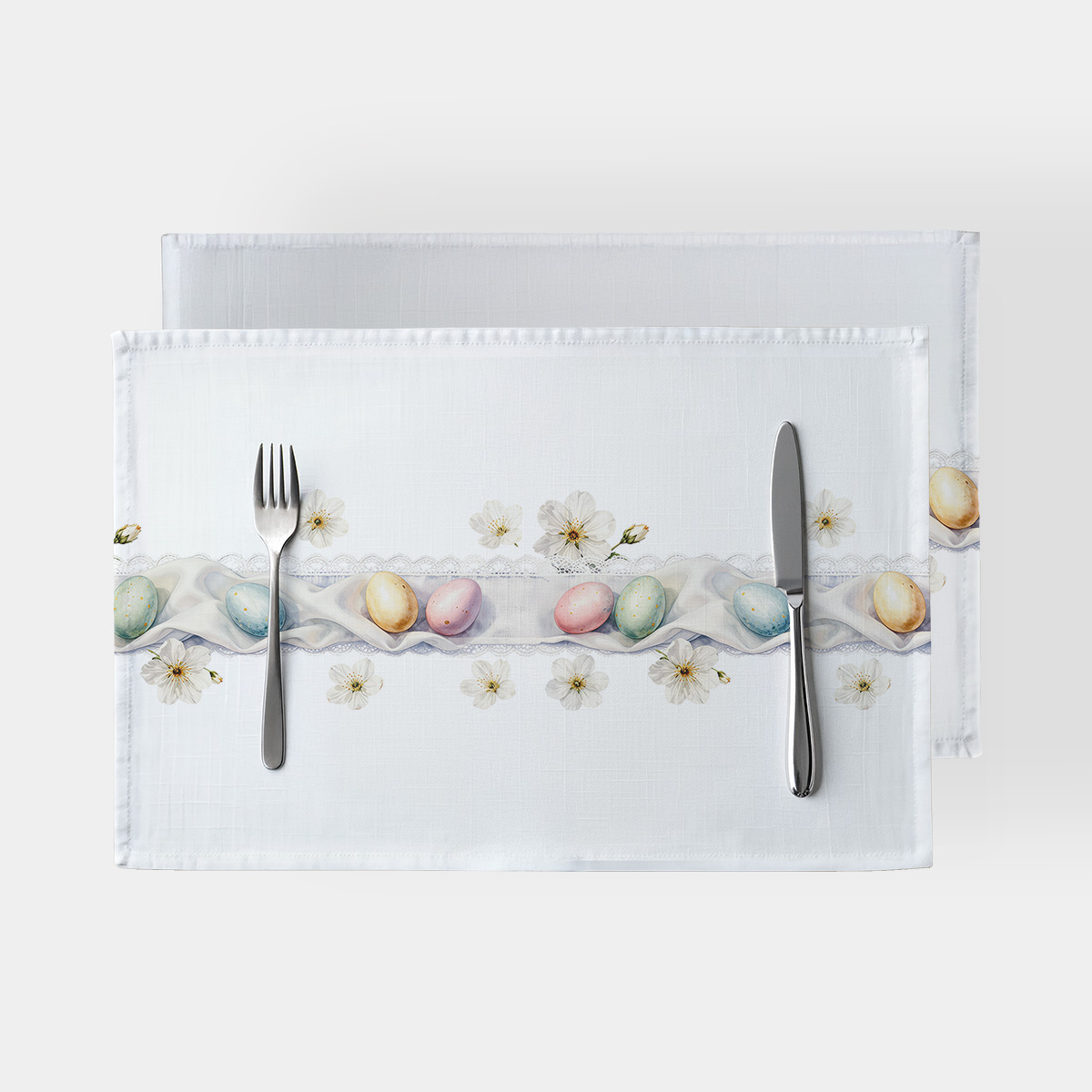 Dwie białe podkładki z motywem pastelowych pisanek i koronkowym paskiem, widok z góry z widocznymi sztućcami