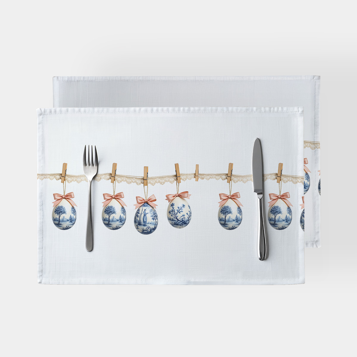 biała podkładka ze wzorem zawieszonych pisanek na koronkowym sznurku ułożona ze sztućcami