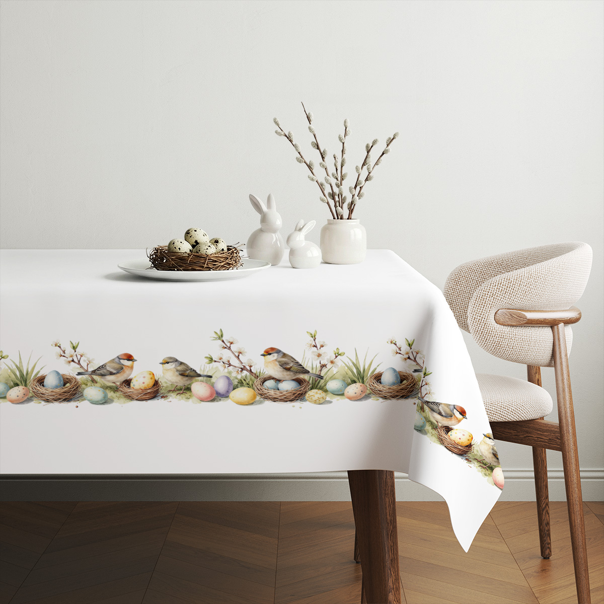 aranżacja stołu z obrusem, koszyk z jajkami i gałązkami bazi tworzą wiosenną dekorację