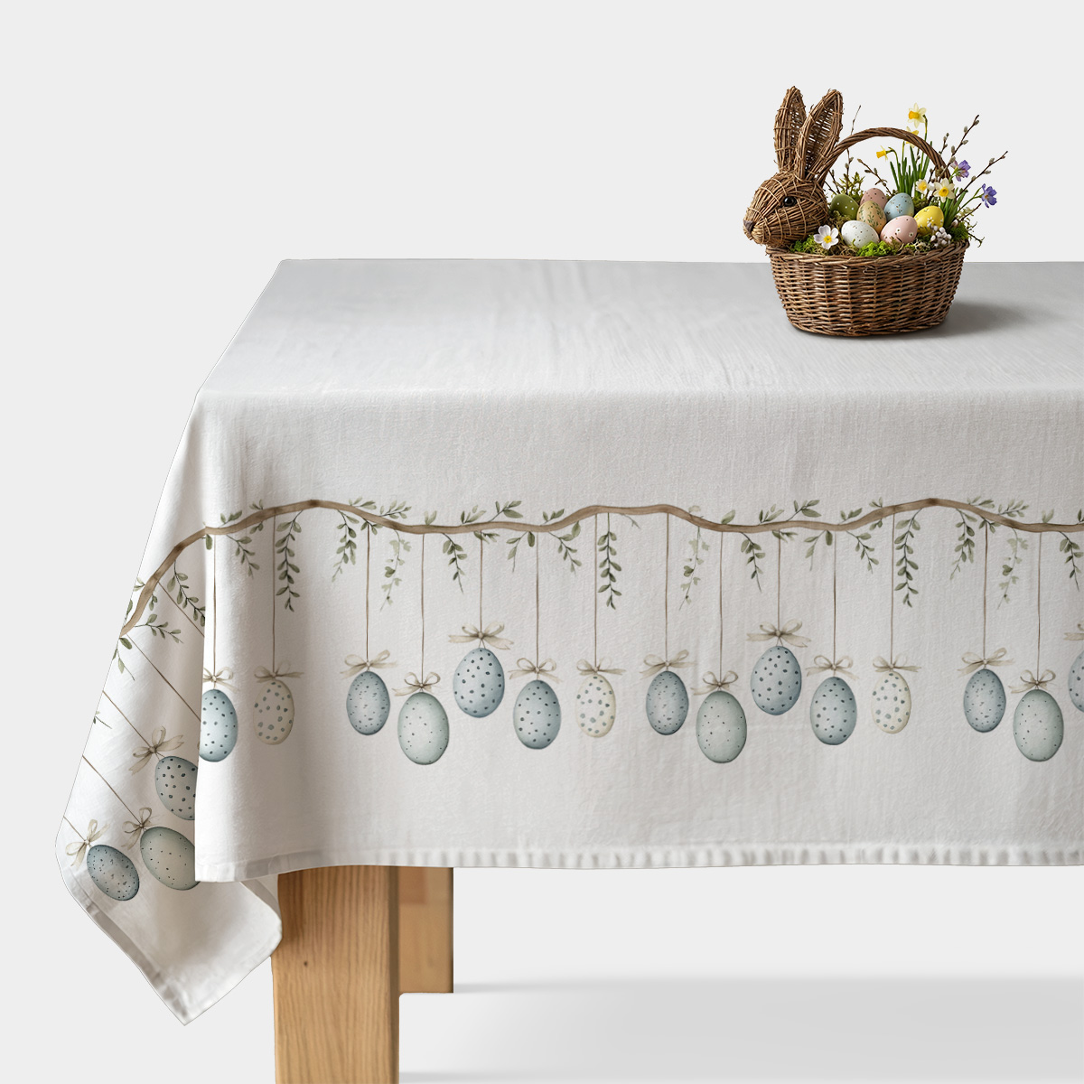 obrus z akwarelowymi wiszącymi jajkami i gałązkami, ujęcie stołu z dekoracyjnym koszykiem z jajkami