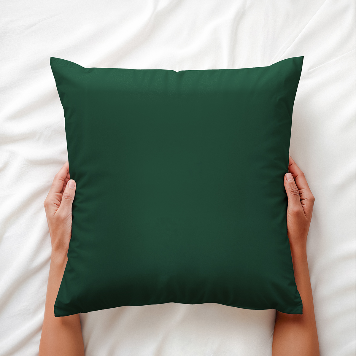 Widok z góry: ręce trzymające poduszkę dekoracyjną w butelkowej zieleni na białej pościeli