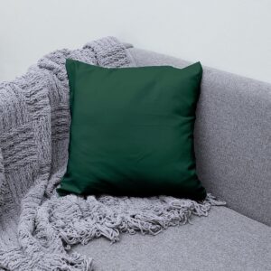 Poduszka dekoracyjna w butelkowej zieleni ułożona na szarej sofie obok plecionego koca