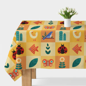 Obrus rozłożony na stole z wzorem kolorowych kwadratów z ptakami, rybkami i biedronkami