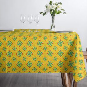 Stół zastawiony talerzami i kieliszkami na żółtym obrusie z turkusowo-czerwonym wzorem