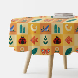 okrągły obrus z kolorowymi kwadracikami ze zwierzątkami i roślinami na stole, ujęcie z boku