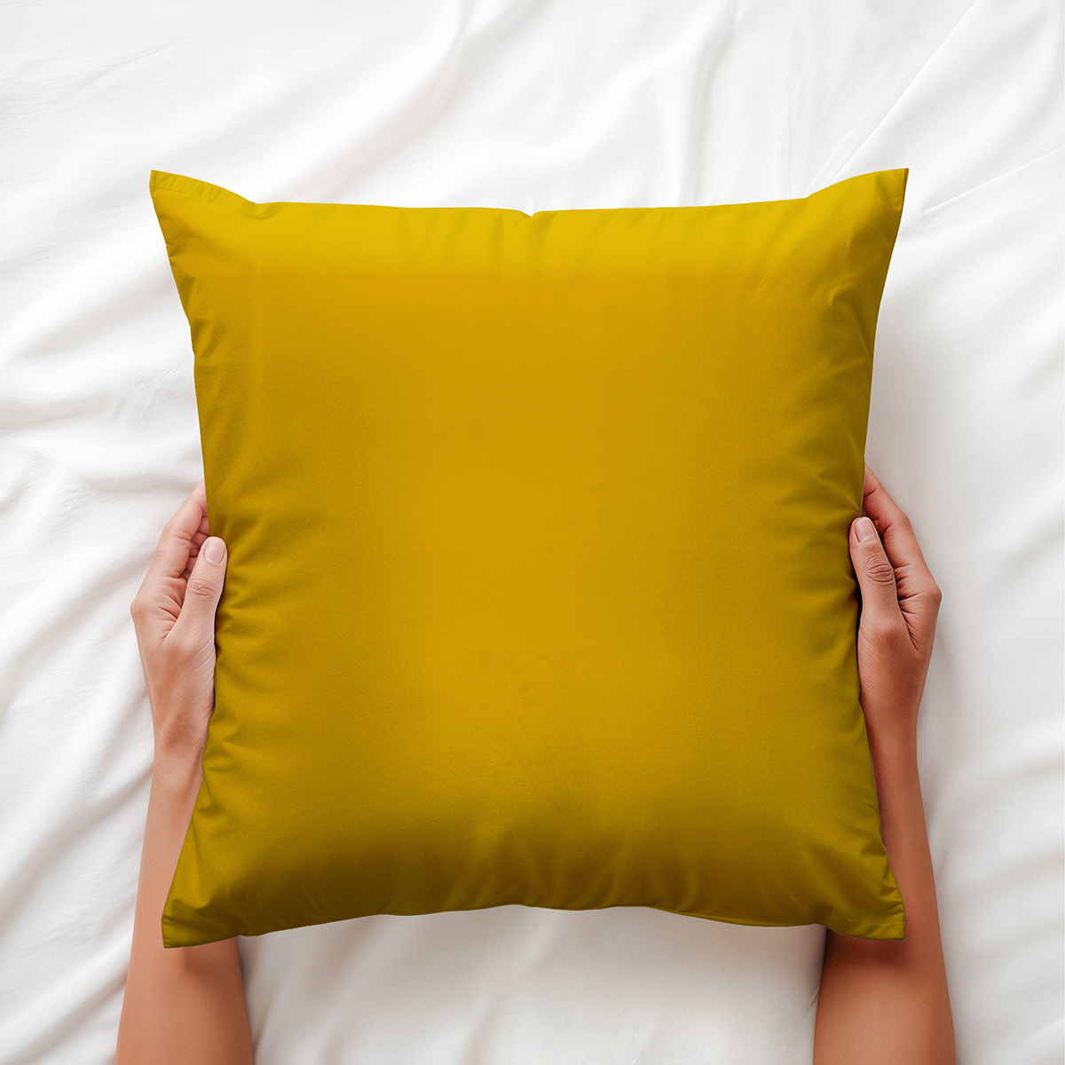 ręce trzymające musztardową poduszkę na białej pościeli