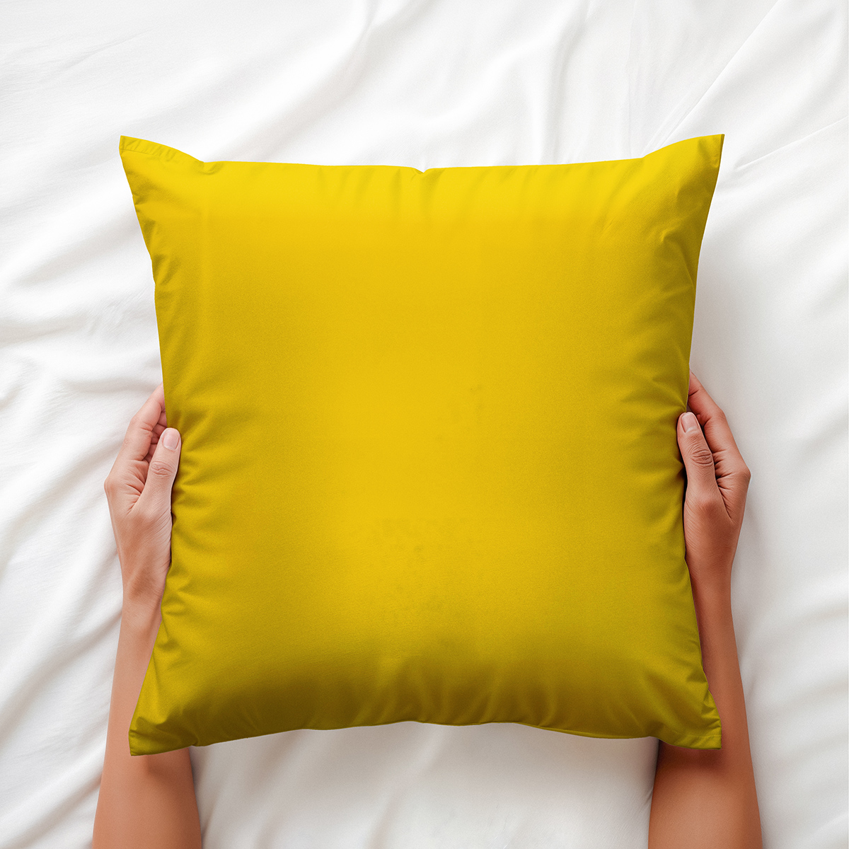 dłonie trzymające żółtą poduszkę na białej pościeli, ujęcie detalu