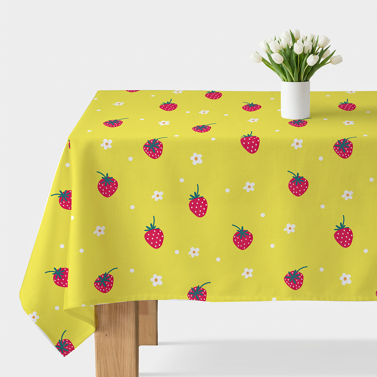 Obrus na stole z nadrukiem czerwonych truskawek i białych kwiatuszków na żółtym tle, widok ogólny