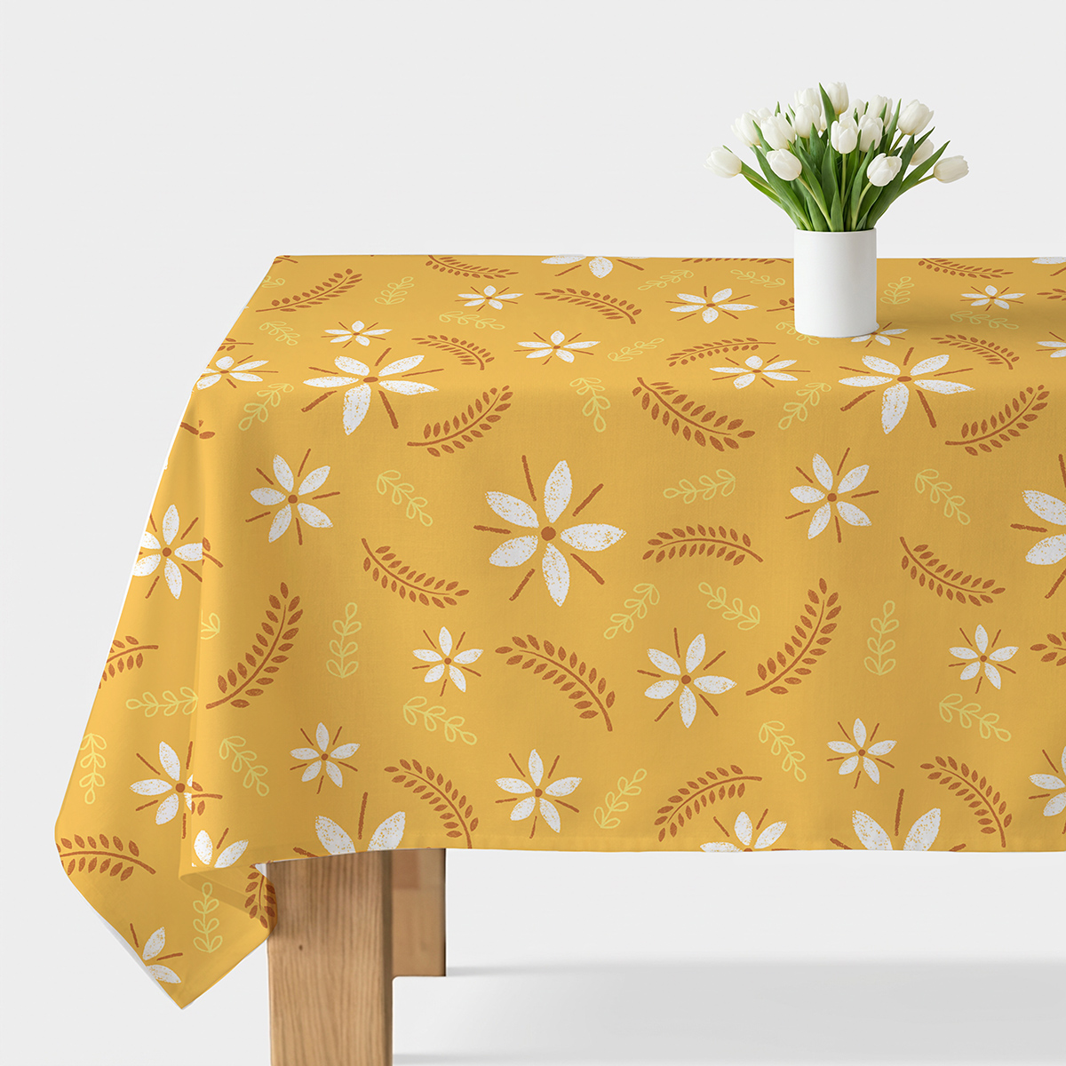 Stół nakryty musztardowym obrusem z białymi kwiatami i wazonem z białymi tulipanami