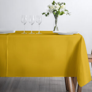 stół nakryty musztardowym obrusem z kieliszkami i białym bukietem