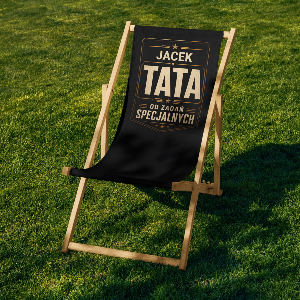 Zbliżenie na złoty nadruk „TATA” i personalizowane imię na czarnym materiale leżaka — close-up personalizacji imienia dla taty